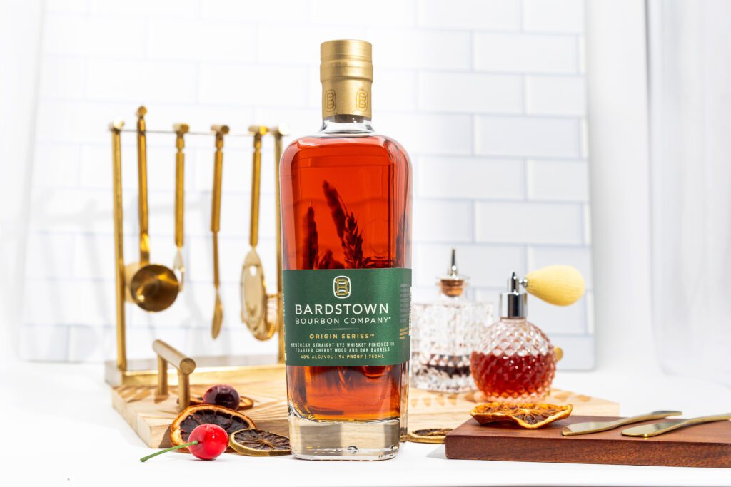 Bottle of Bardstown Bourbon Company Origin Series Kentucky Straight Rye Whiskey, set on a bar counter with cocktail tools and garnishes in the background.